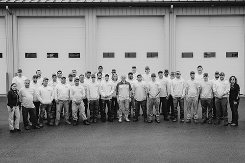 Bob Emi and a group of volunteers pose for a photo in front of an industrial garage