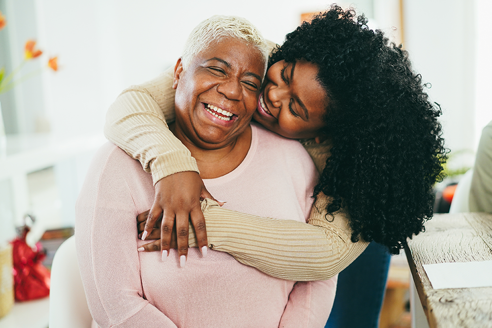 Memorial Fund A young black woman hugs an older black woman in a pink shirt from behind