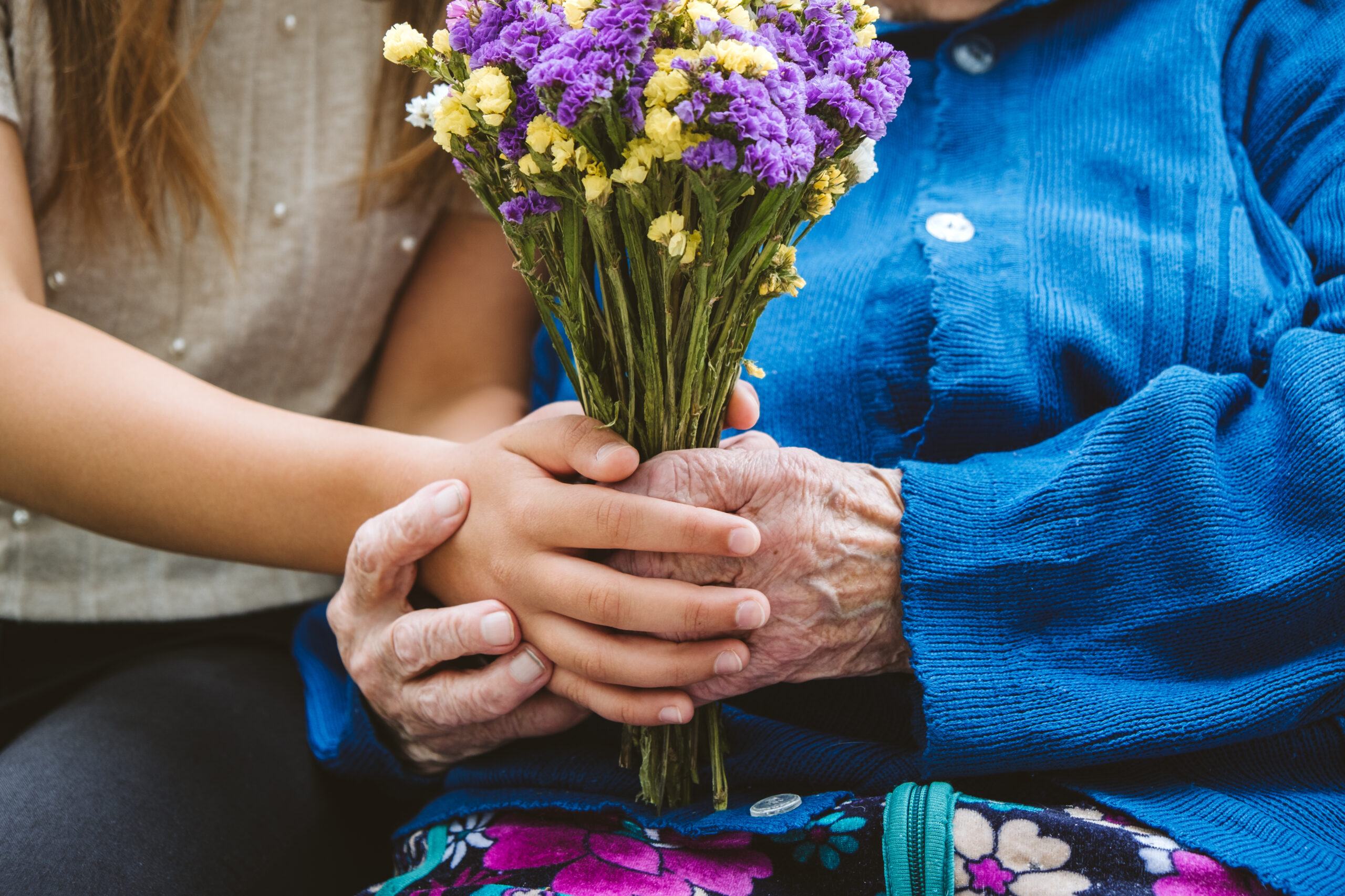 Memorial Fund A young white woman and elderly woman hold hands around a bouquet of flowers