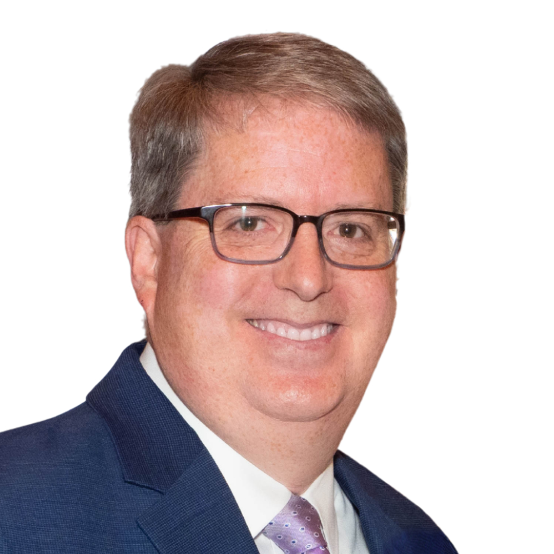 A white man with light hair, thick dark glasses, in a blue suit with a purple tie