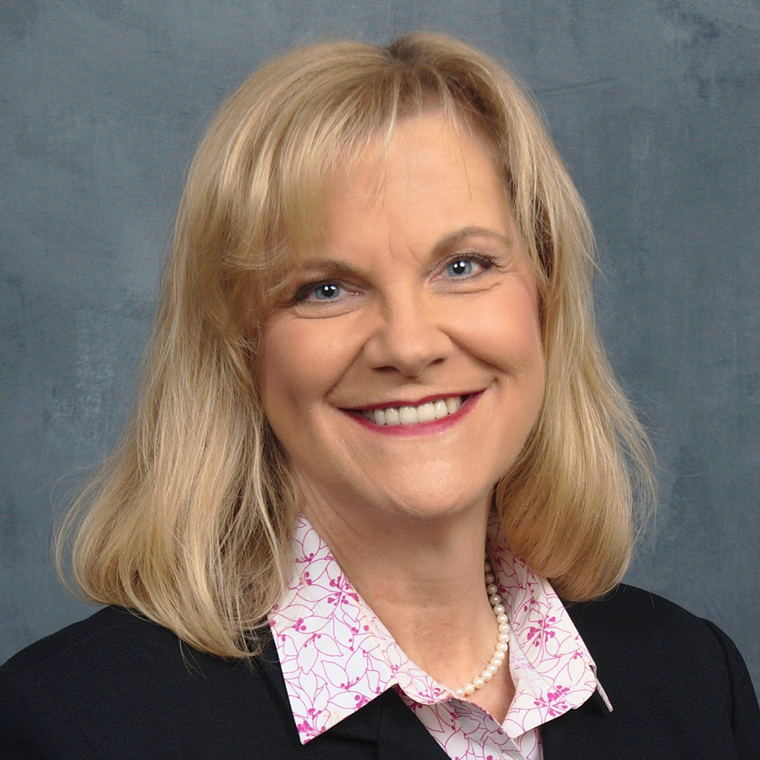 A white woman with fair hair in a dark sweater with a pink collar