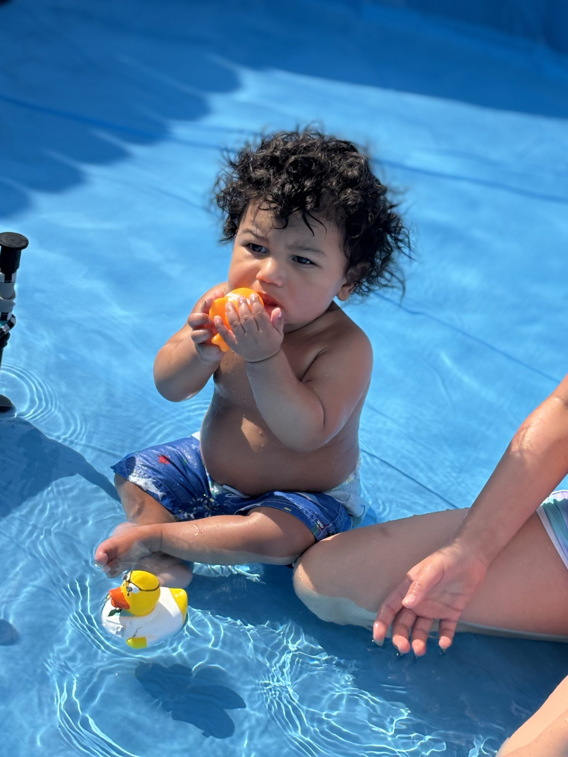 baby boy with curly hair playing with pool toy