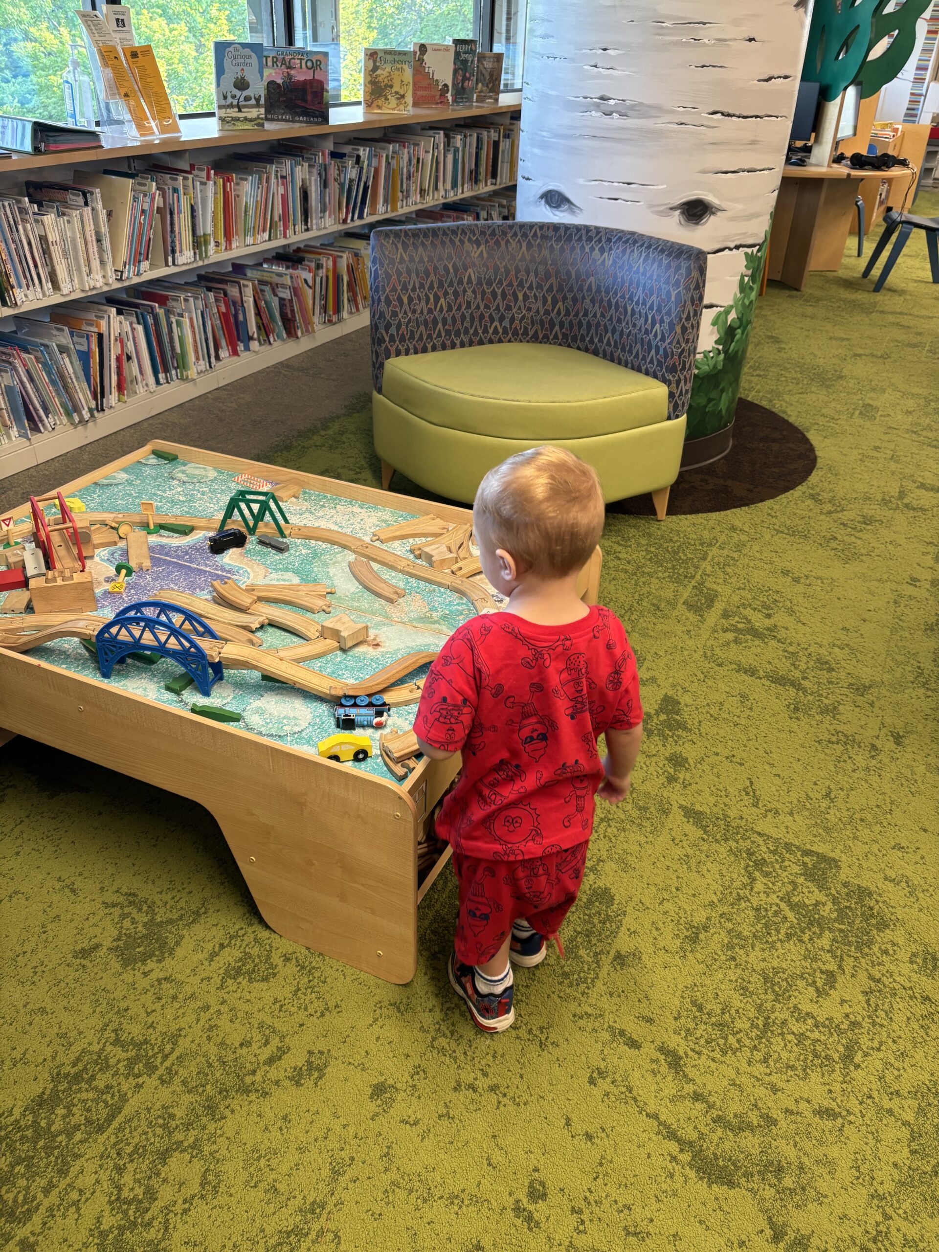 toddler boy playing with train table at a library