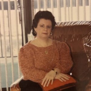 JoAnn Barbara Faitt-Jacobs, a white woman with dark hair, a maroon shirt sitting in front of a window with blinds