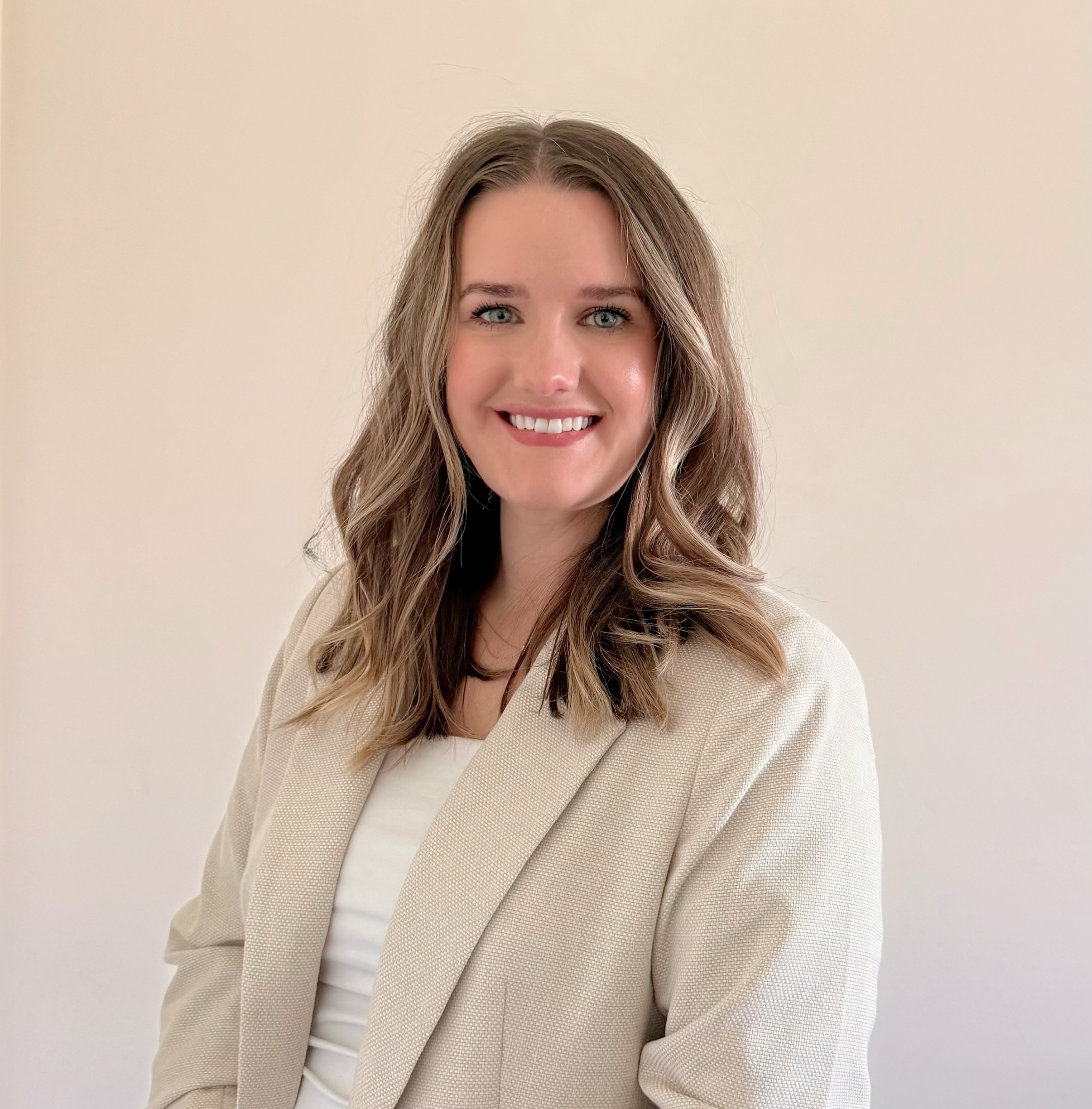 Claudia Panichelli, a white woman with brown hair and blonde highlights wears a tan jacket while smiling against a light background