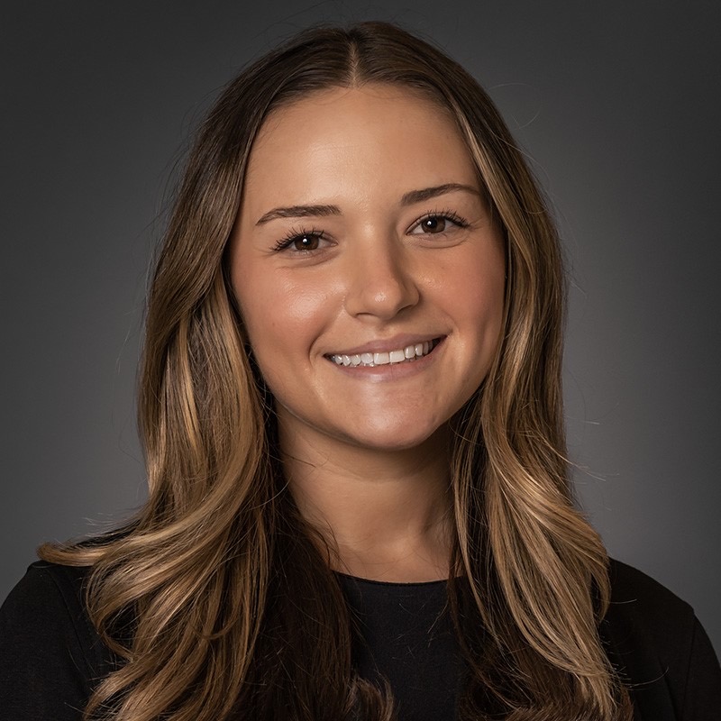 Madison Dill, a white woman with medium-long light brown hair smiles against a dark background