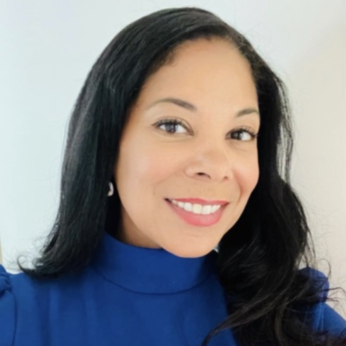 Maia Green, a woman with long dark hair and a blue sweater smiles against a light background.